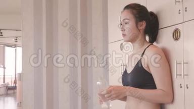 运动亚洲妇女打开更衣室的私人<strong>储物</strong>柜，并在运动中放松休息后放置饮用纯净水<strong>瓶</strong>